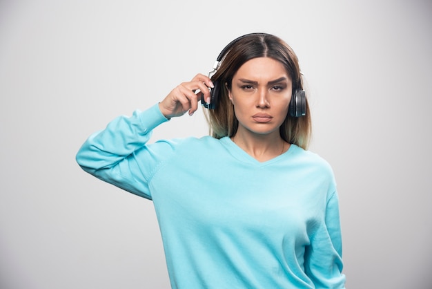 Chica rubia en sudadera azul con auriculares y tratando de entender la música.