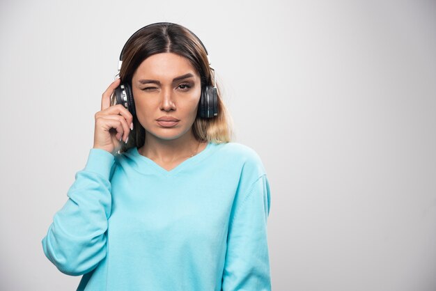 Chica rubia en sudadera azul con auriculares y tratando de entender la música.