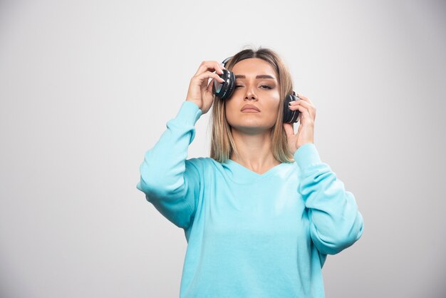 Chica rubia en sudadera azul posando con auriculares.