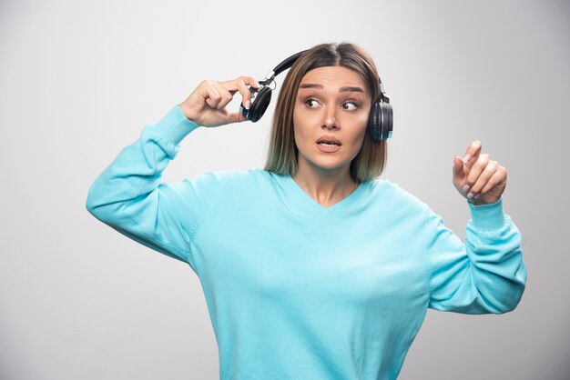 Chica rubia en sudadera azul sacando los auriculares para escuchar a la gente alrededor.