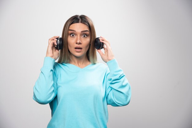 Chica rubia en sudadera azul sacando los auriculares para escuchar a la gente alrededor