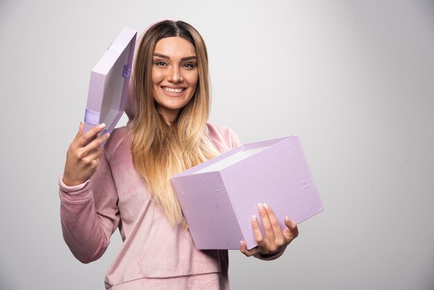 La chica rubia en sudadera recibió una caja de regalo y se siente realmente sorprendida.