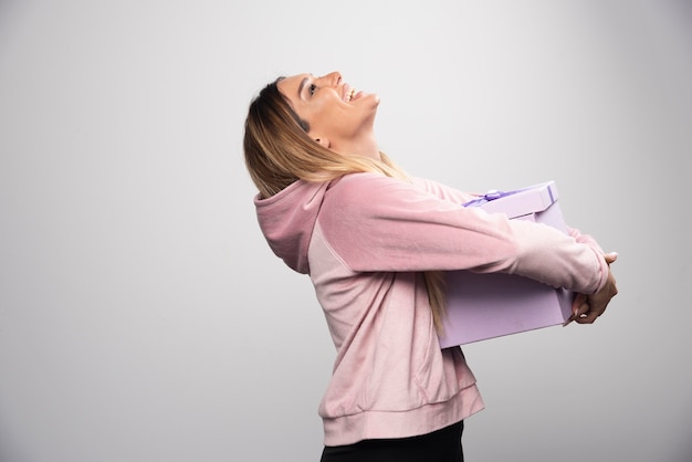 La chica rubia en sudadera recibió una caja de regalo y se siente realmente sorprendida.