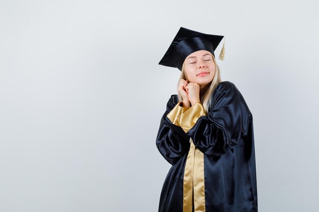 Chica rubia en toga de graduación y gorra estrechando las manos y luciendo linda