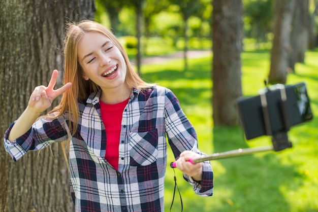 Chica rubia tomando una selfie junto a un árbol