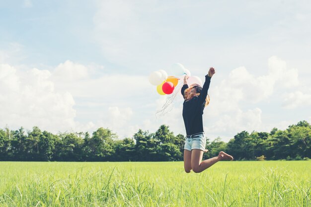 Chica saltando con globos sobre el campo verde