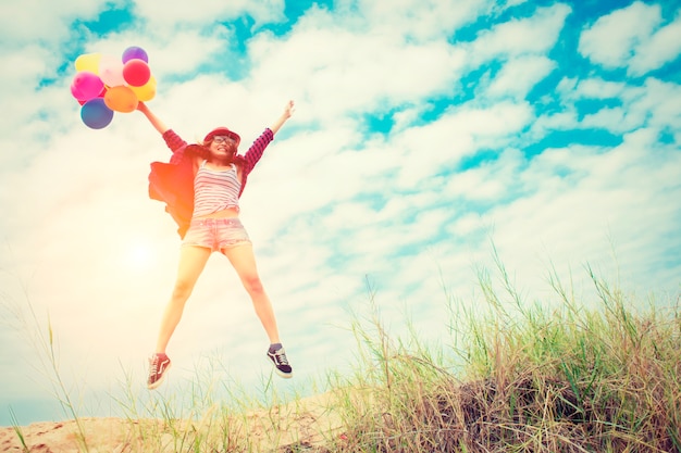 Chica saltando en la playa con globos de colores