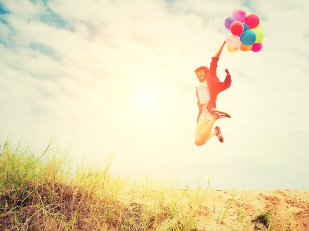 Chica saltando en la playa con globos