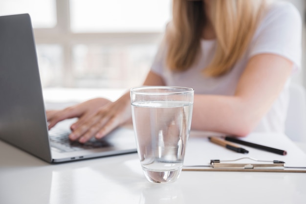 Chica sana usando el portátil con vaso de agua