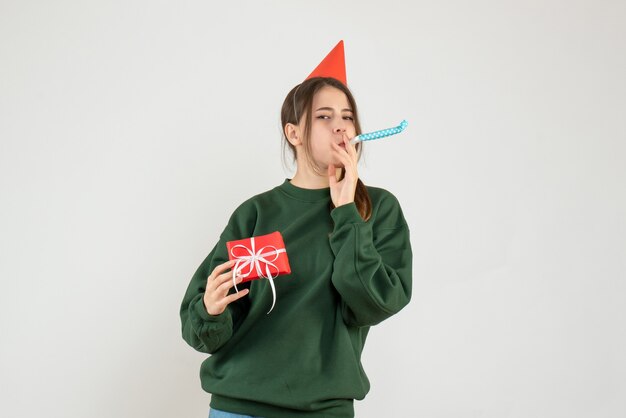 Chica satisfecha con gorro de fiesta sosteniendo su regalo de Navidad con matraca en blanco