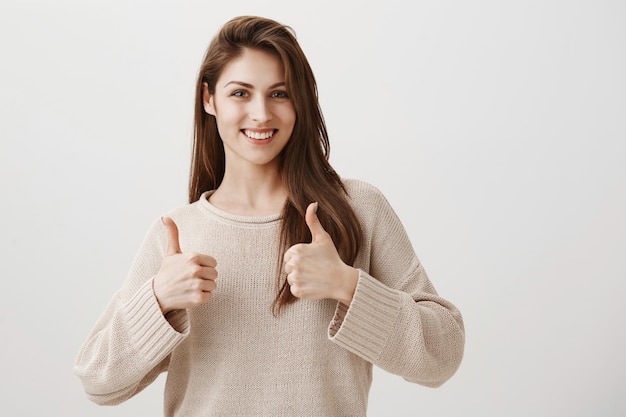 Chica satisfecha mostrando gesto pulgar hacia arriba bien hecho, sonriendo complacido