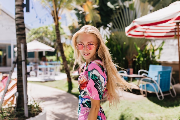 Chica segura en ropa de verano mirando por encima del hombro con bonita sonrisa.