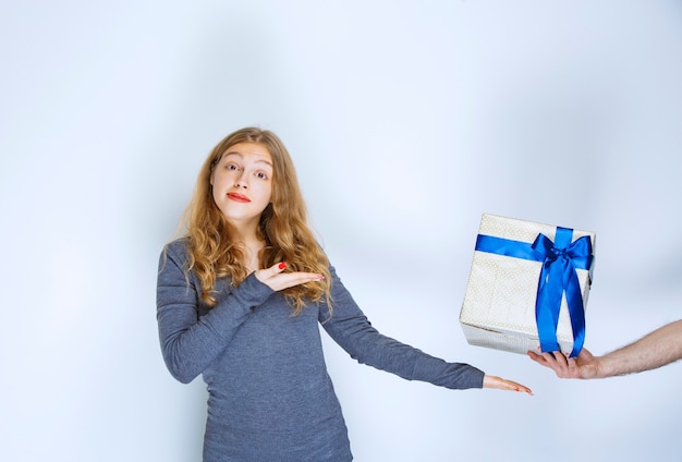 Chica señalando una caja de regalo azul blanca que se le ofrece.