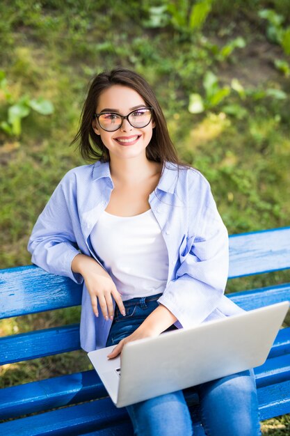 Chica sentada en el banco en el parque y usa su computadora portátil