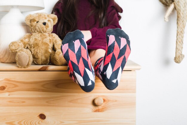 Chica sentada cerca de peluche mostrando sus pies con calcetines multicolores