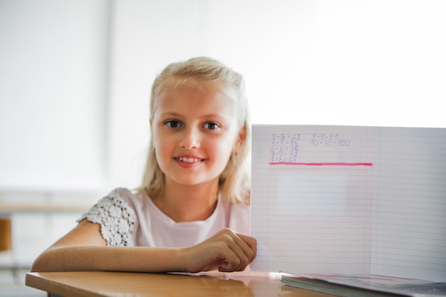 Chica sentada en la mesa de la escuela con el cuaderno