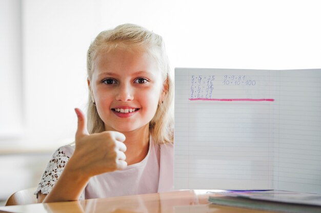 Chica sentada en la mesa de la escuela con el cuaderno