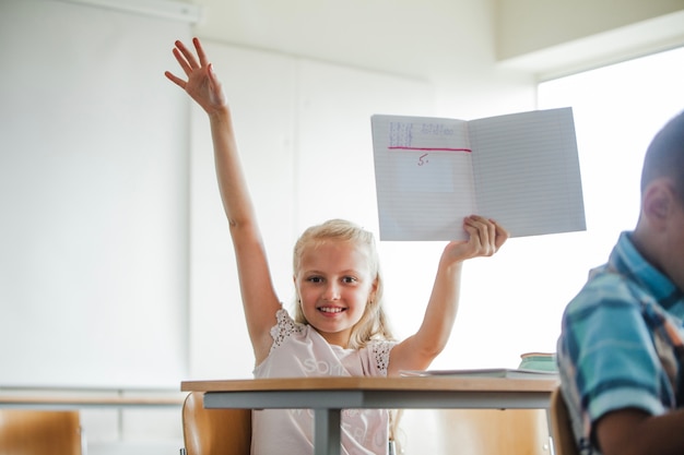 Chica sentada en la mesa de la escuela con el cuaderno