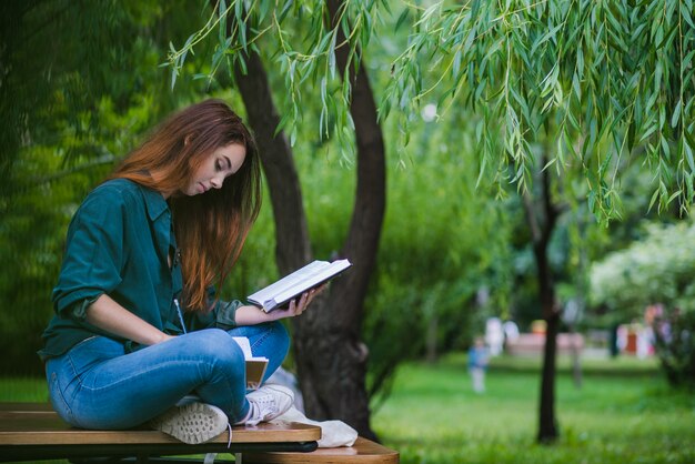 Chica sentada en la mesa en el parque de la escritura