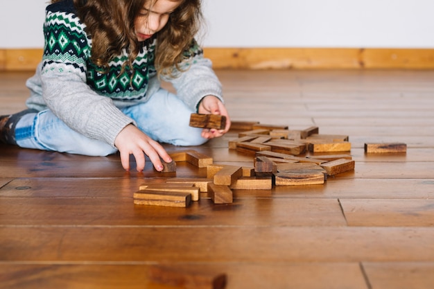 Chica sentada en el piso de madera jugando al juego jenga