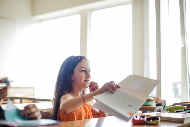 Foto gratuita chica sentada en la sala de clase sosteniendo el cuaderno