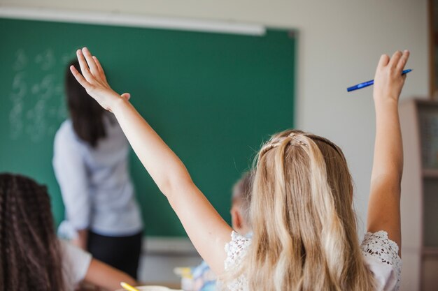 Chica sentada en el salón de clase levantando las manos