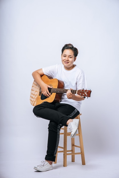 Chica sentada en una silla y tocando la guitarra.