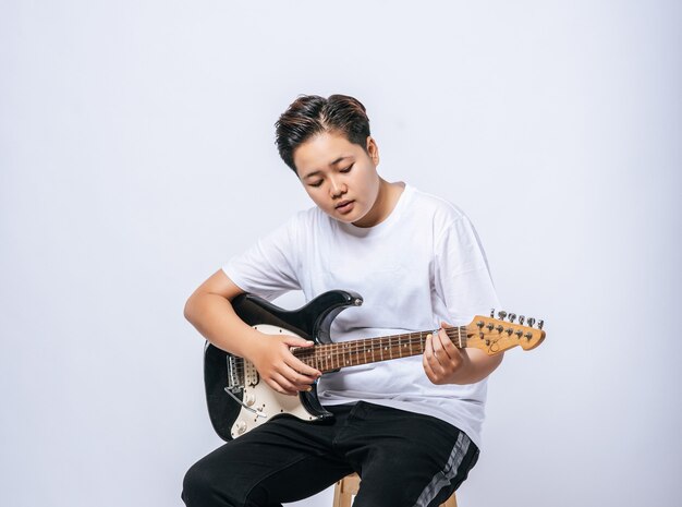 Chica sentada en una silla y tocando la guitarra.