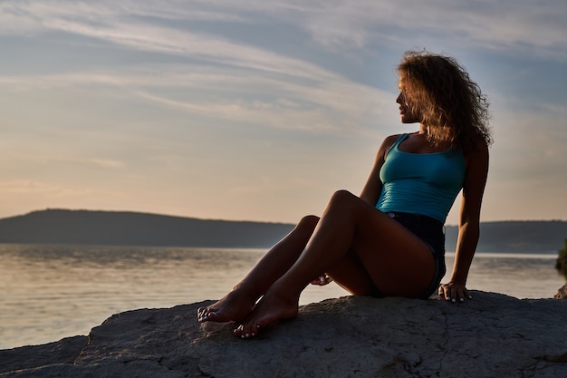 Chica sentada sobre piedras y admirando el paisaje