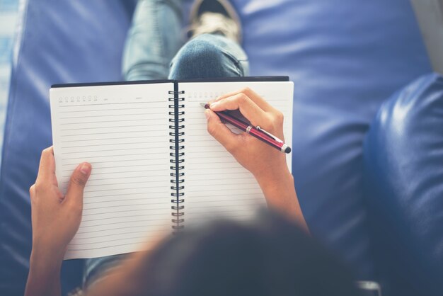 Chica sentada en un sofá escribiendo sobre una libreta