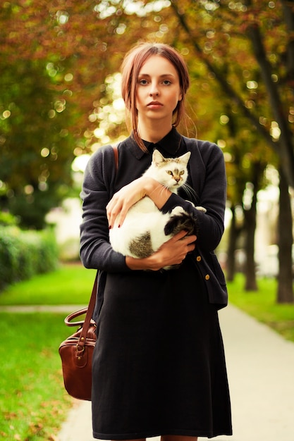 Chica seria abrazando a su gato en el parque