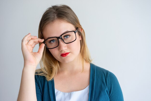 Chica seria con labios rojos ajustando anteojos