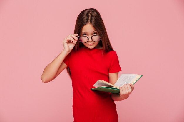 Chica seria nerd en vestido mirando a través de lentes mientras lee