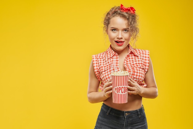 Chica sexy con lazo rojo de pelo rizado con cubo de palomitas de maíz