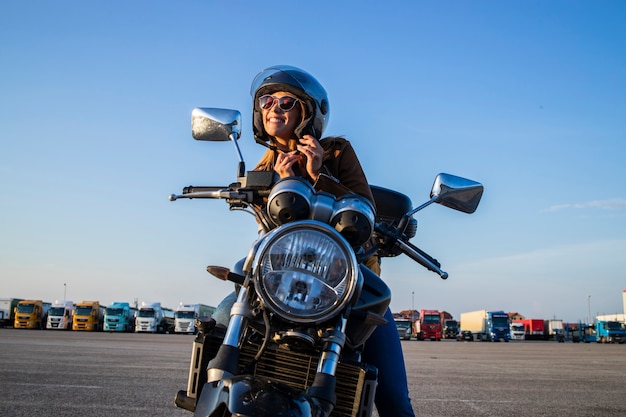 Chica sexy sentada en una motocicleta de estilo retro y abrocharse el cinturón del casco antes de viajar