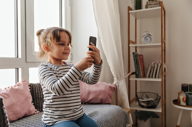 Foto gratuita la chica se sienta en el sofá y se toma una selfie junto a la ventana