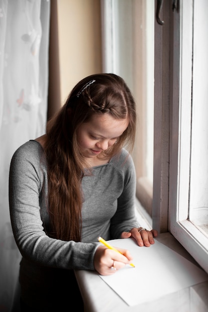 Foto gratuita chica con síndrome de down dibujo junto a la ventana