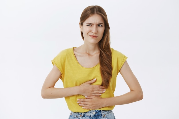 Foto gratuita chica sintiéndose enferma, tocando el estómago y quejándose de calambres o dolor