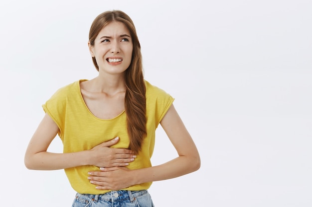 Chica sintiéndose enferma, tocando el estómago y quejándose de calambres o dolor