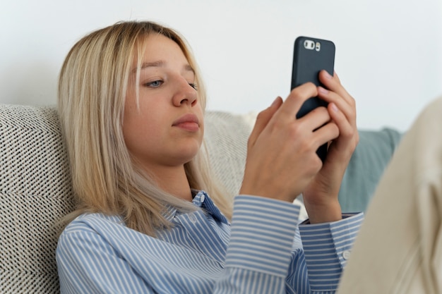 Chica en el sofá con plano medio de teléfono inteligente