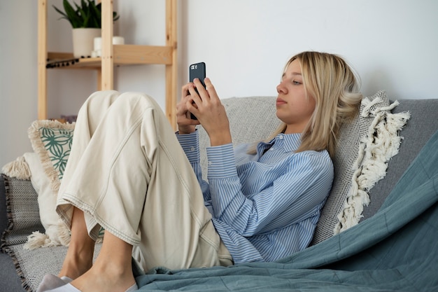 Chica en el sofá con teléfono inteligente de tiro completo