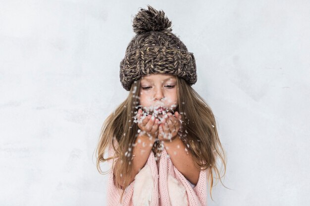 Chica con sombrero de invierno que sopla nieve