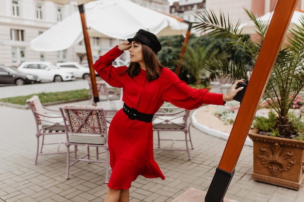 Chica soñadora de 24 años mira a la distancia con esperanza Foto en ciudad europea de modelo elegante con gorra negra cálida