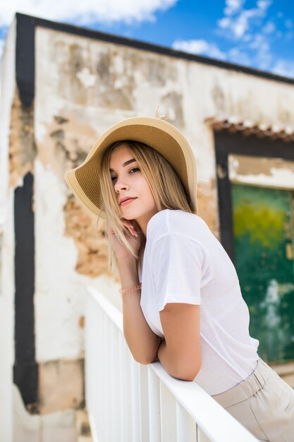 Chica soñadora sentada en la terraza con sombrero de paja y gafas de sol.