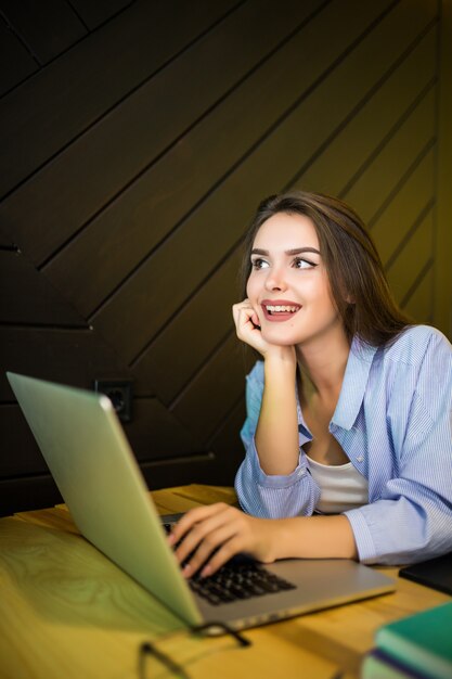 Chica soñando está trabajando en la computadora portátil en el café