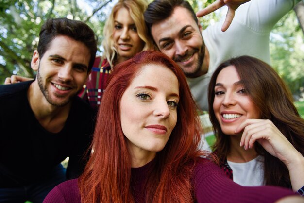 Chica sonriendo haciendo una autofoto con sus amigos alrededor