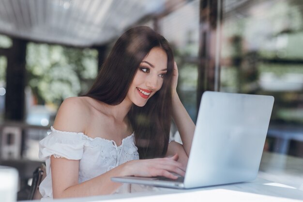 Chica sonriendo con los labios pintados de rojo escribiendo en un portátil