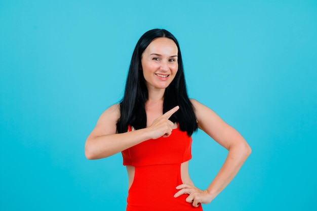 Chica sonriente apunta a la derecha con el dedo índice sobre fondo azul.