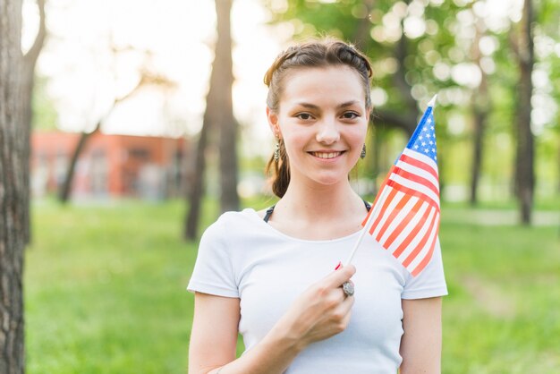 Chica sonriente con bandera americana en la naturaleza