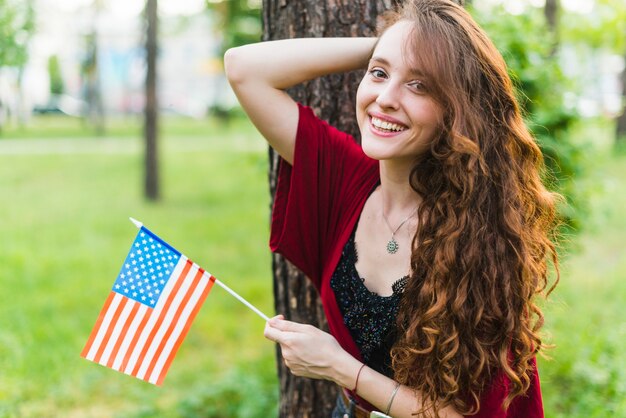 Chica sonriente con bandera americana en la naturaleza